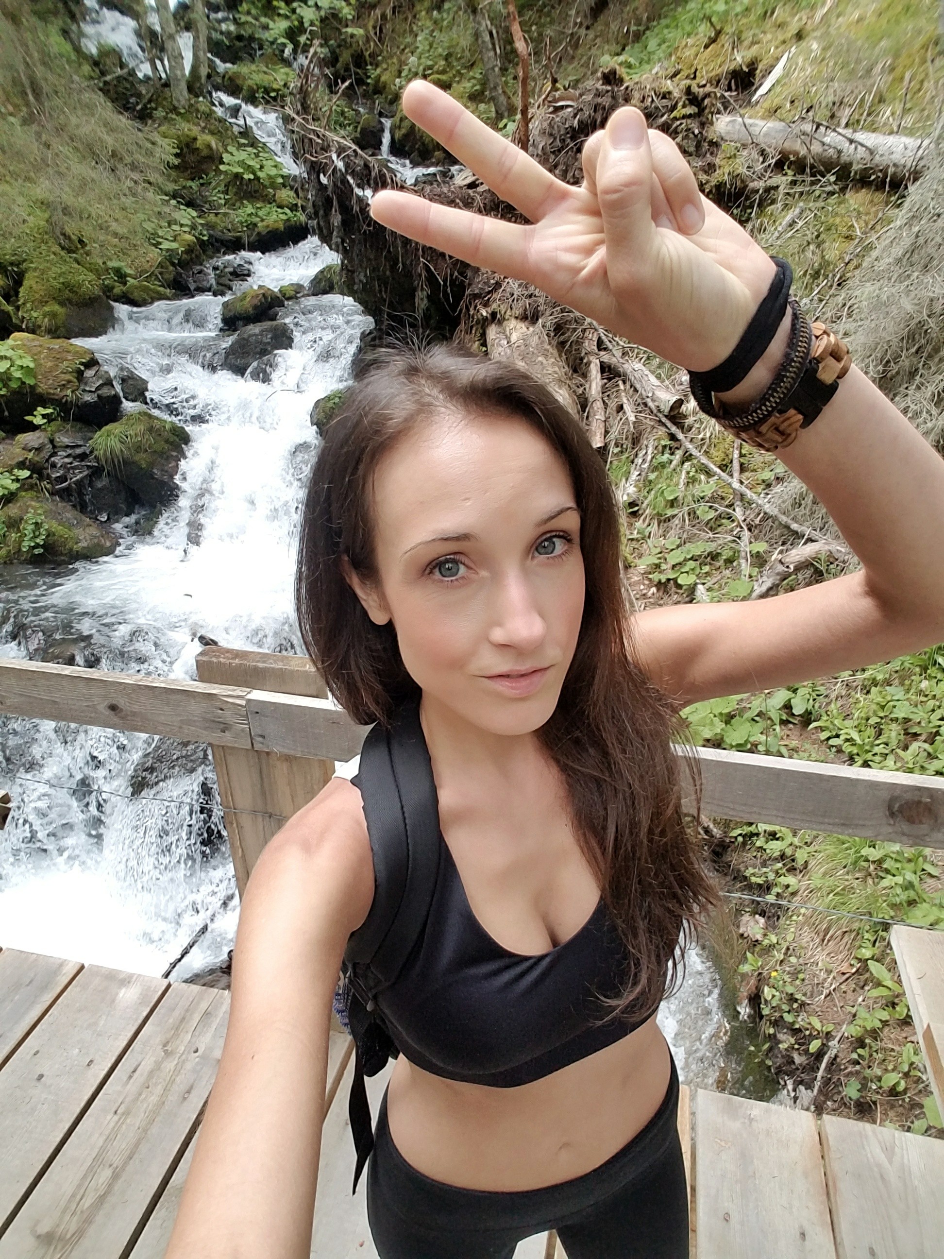 Woman hiking by a waterfall and giving a peace sign