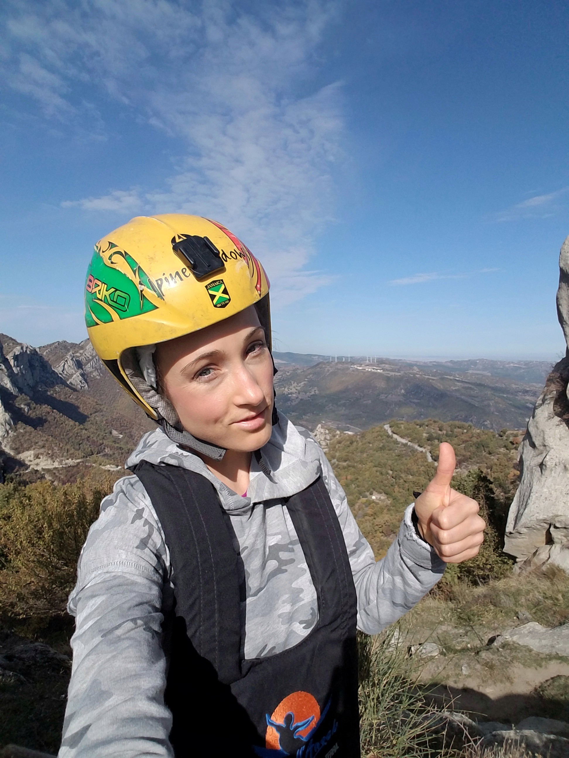 Woman with a helmet and harness standing in front of a valley