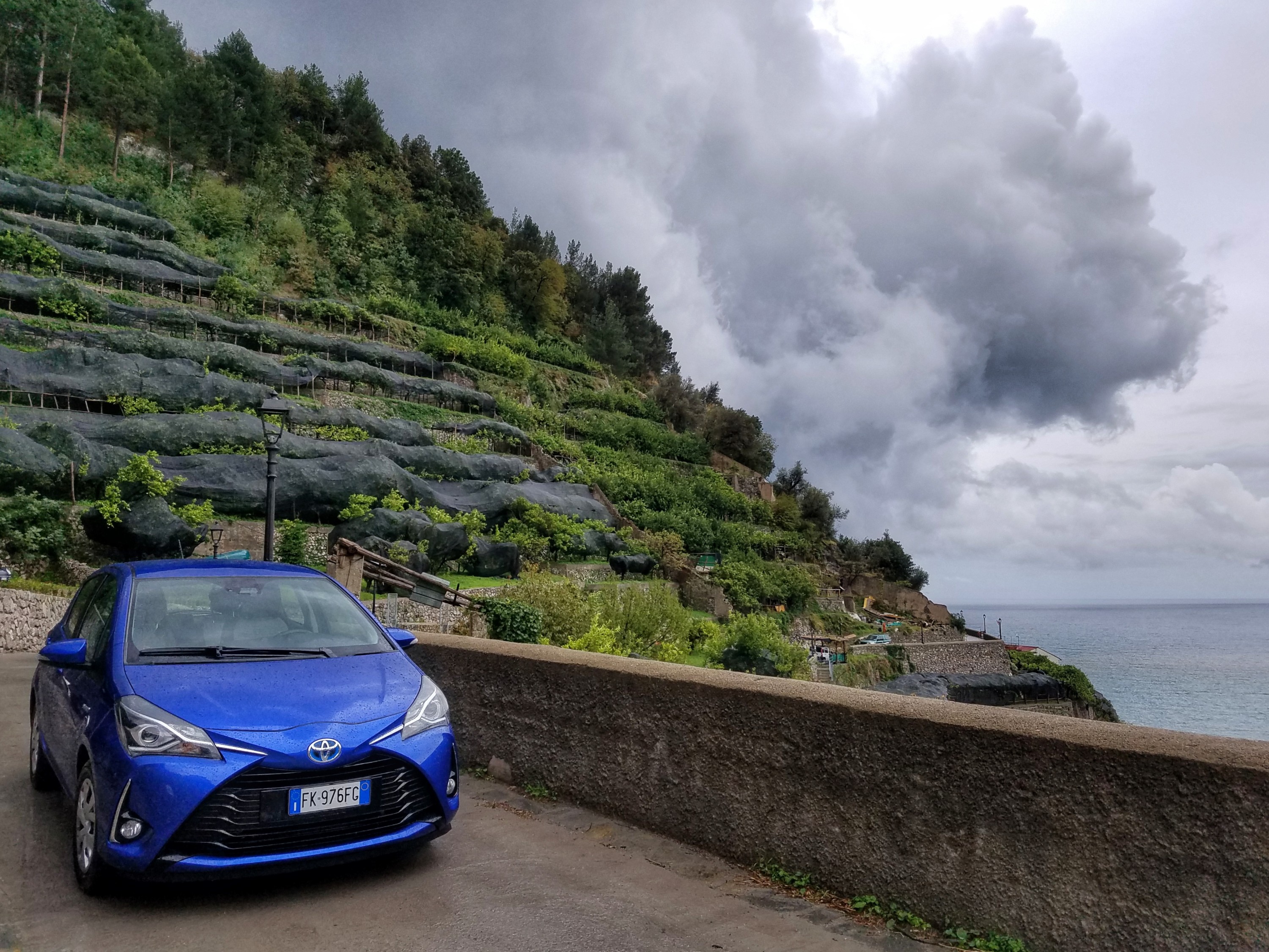 Blue Toyota parked on a road with a hillside and water in view