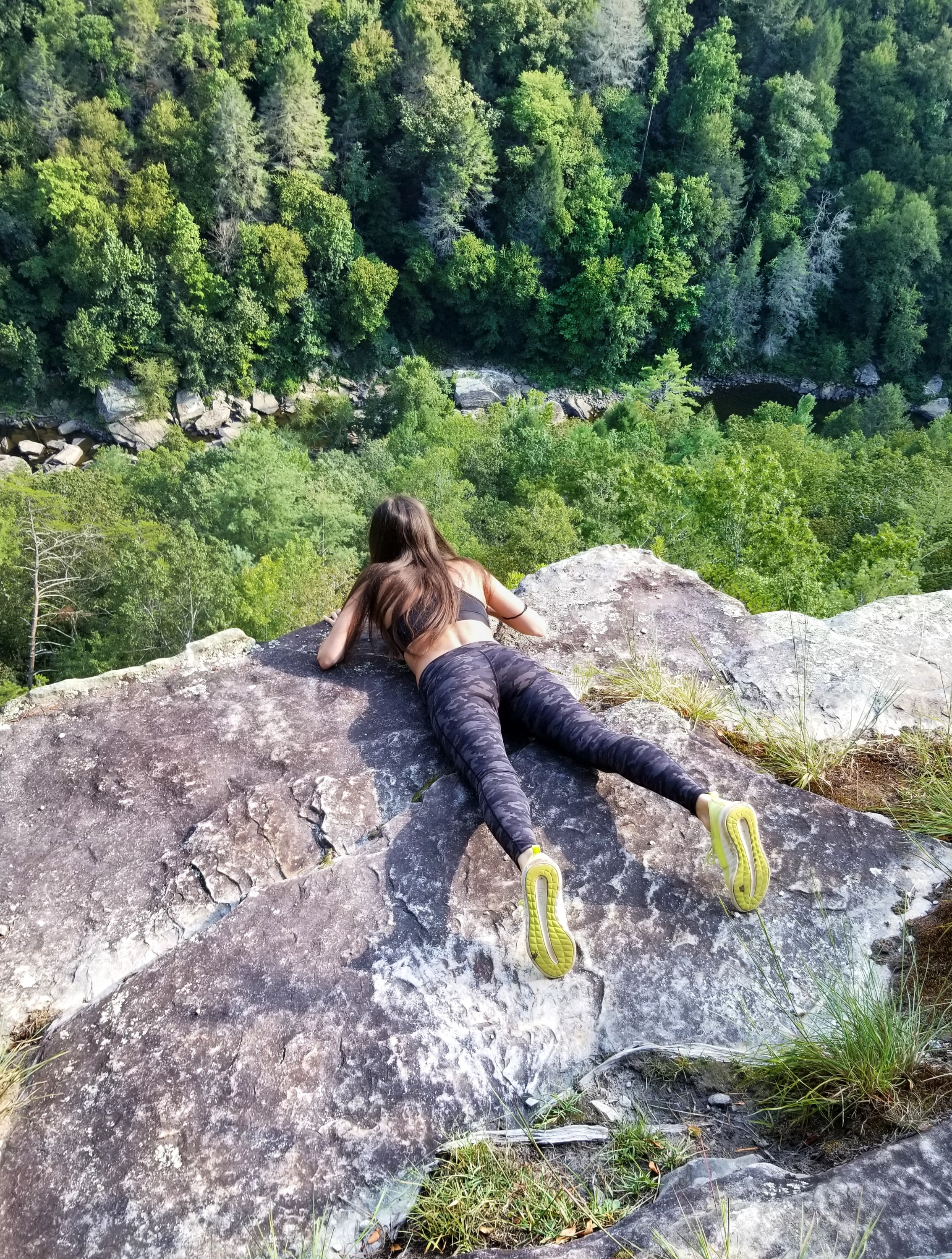 Woman laying on her stomach and peeking over the edge of a cliff