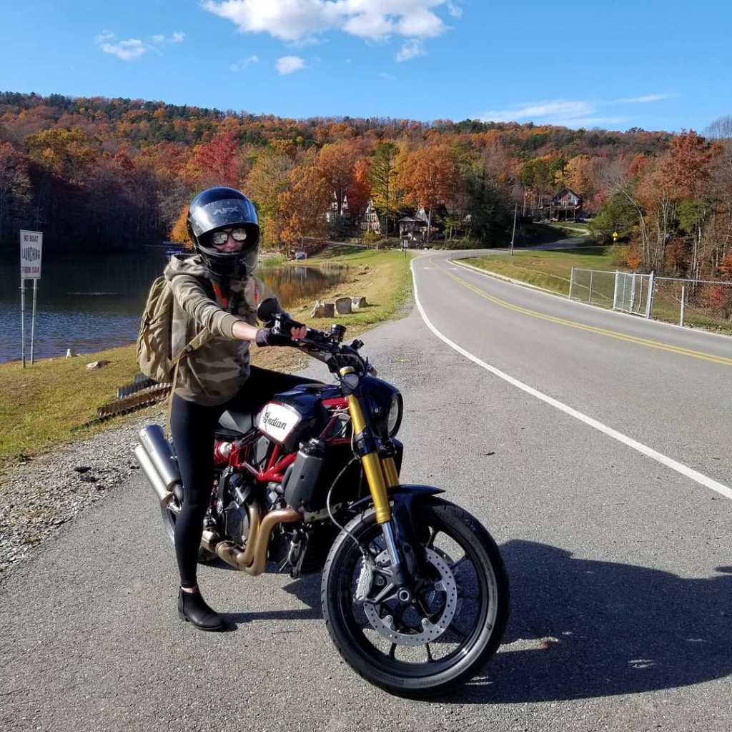 Woman on motorcycle parked on roadway surrounded by fall foliage 
